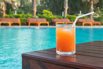 Summer Vacation Concept : Welcome drink orange juice punch put on wooden table nearly swimming pool with blue water and daybed in background.