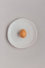 A brown egg on a beige plate on beige background, top view, copy space