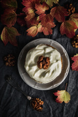 An autumnal stylized image of a carrot cake with cream and walnut, colourful leaves, dark grey background, film grain effect.