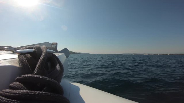POV motorboat's bow speeding across the water, anchor mount with a bowline, an island in the Adriatic Sea in background