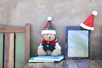 Teddy bear with tablet and santa hat on table