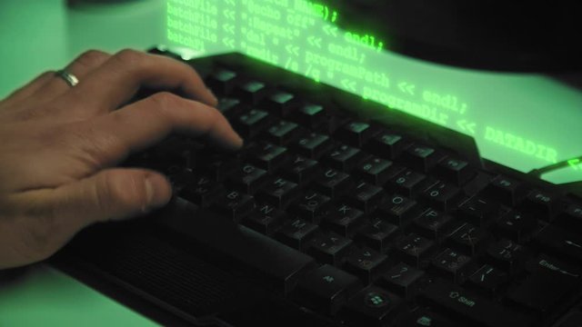 Сlose-up of hacker hands while green code characters fly out of the keyboard in the dark office room. 4K (UHD)