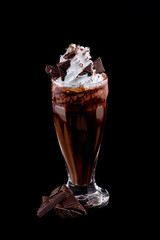 Closeup vertical glass of chocolate milkshake decorated with whipped milk isolated at black background.