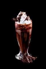 Vertical image of glass of chocolate milkshake decorated with whipped milk isolated at black background.
