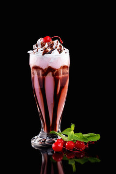 Closeup vertical glass of cherry with cholocate milkshake decorated with mint isolated at black background.