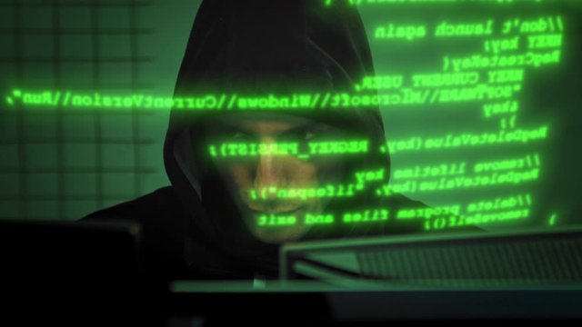 Close-up of male hacker working on a computer for cyber attack while green binary hacking code characters running in front of him in a dark office room. Motion graffic. 4K (UHD)