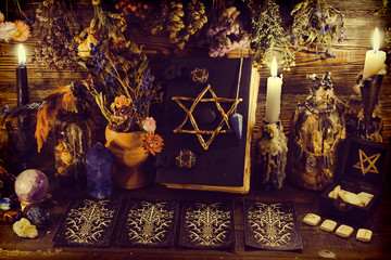 Creepy witch book with pentagram, tarot cards, runes, gemstone, candle and magic objects.