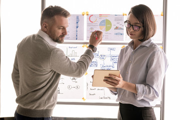 Serious businessman looking at display of touchpad held by his colleague