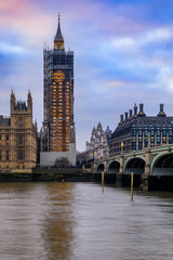 Big Ben covered in scaffolding for restoration and Portcullis House across Thames river before sunset in London, England