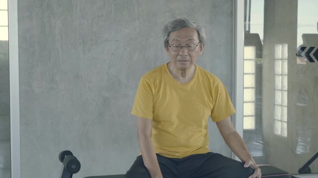 Asian old man tired after effort exercise in the gym, asia senior sweat sitting expression exhausted and breathing after workout in the fitness, lifestyle of healthy and wellness concept.