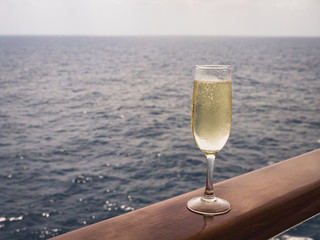 Beautiful champagne glass on the open deck of a cruise liner against the backdrop of blue sea waves. Side view, close-up. Concept of leisure and travel