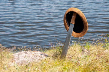 Fototapeta premium hat worn on a sword stuck in the ground on the shore of the pond