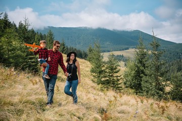 family walk on the field near the mountains in sunny day yellow grass father mother son holding hands on the sunset