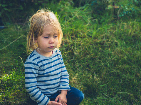 Little toddler sitting on the lawn in garden