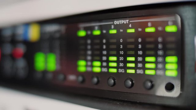 Audio equalizer bars moving on electronic panel, music control levels on desk, close up. Blurred bokeh background.