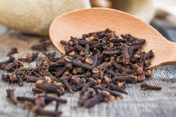 A spice of dried cloves lies on a wooden spoon and is scattered on old wooden boards.