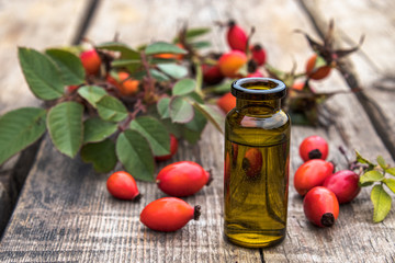 Glass bottle of rosehip seed essential oil with fresh fruits on a wooden table. Tincture or essential oil with rose hips.