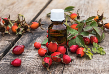 Bottle of rosehip seed essential oil and fresh red berries on a wooden table. Tincture or essential oil with rose hips.