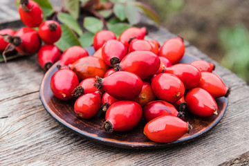 Fresh red rose hips and green leaves on a bowl on a wooden table.