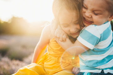 Close up of a lovely little kid embracing his sister with love against sunset outdoor in a field of...