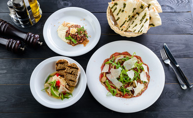 three-course cuisine, carpaccio, tartar and seafood, a set of dishes for dinner on a black table of a restaurant