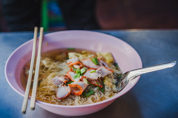 Egg noodle soup with red roasted pork and shrimp wonton in bowl at noodle shop street food.
