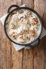 Tasty meatballs with mushrooms served in a creamy sauce with thyme close-up in a pan. Vertical top view