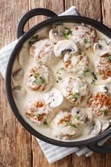 Fried meatballs with mushrooms in a gentle creamy sauce with thyme close-up in a pan. Vertical top view