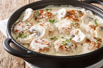 Main dish of meatballs with mushrooms served in creamy cheese sauce with thyme close-up in a pan on the table. horizontal