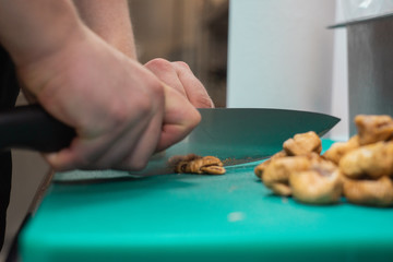 Cook in a restaurant slicing dried figs with a knife on a green teflon cutting board CLOSE UP