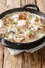 Fried meatballs with mushrooms in a gentle creamy sauce with thyme close-up in a pan. vertical
