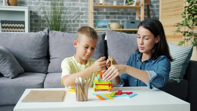 Slow motion of loving young lady playing with happy child at home building with blocks enjoying game with boy. Childhood, parenthood and family concept.