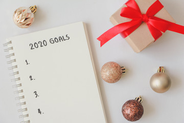 Top view of 2020 goals on notebook with gift box on white background,office desk.