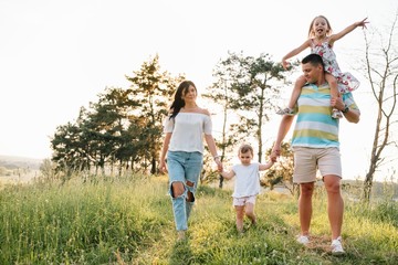 Color photo of smiling young parents and two children, rest and have fun in nature. Love, family and happy childhood lifestyle concept