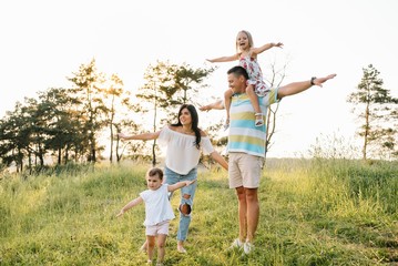 Color photo of smiling young parents and two children, rest and have fun in nature. Love, family and happy childhood lifestyle concept