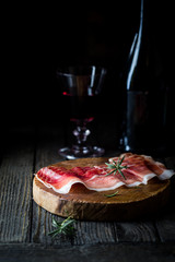 Italian prosciutto crudo or jamon with rosemary over dark wooden background. Raw ham.