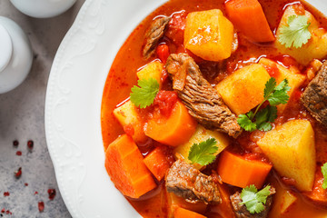 Traditional hungarian goulash. Beef stew with potatoes, carrots and paprika in white plate, top view.