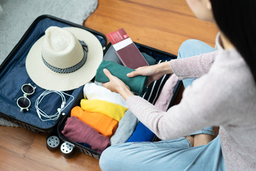Preparing suitcase for summer vacation trip. Young woman checking accessories and stuff in luggage on the bed at home before travel.