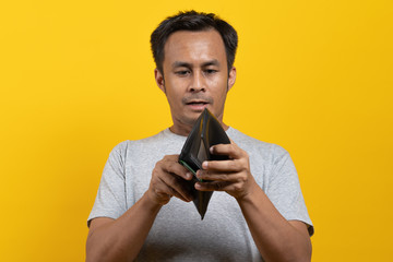 Financial bankruptcy man opening empty wallet isolated on yellow background.