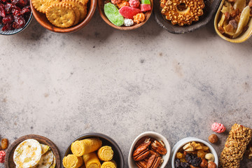 Variety of snacks and sweets on gray background. Waffles, nuts, sweets, cookies, chips and fruits, top view.