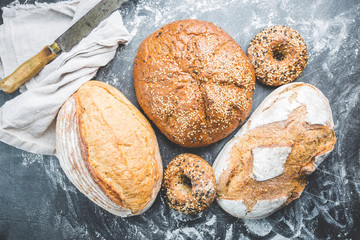 Assortment of fresh baked bread and buns on black background, top view