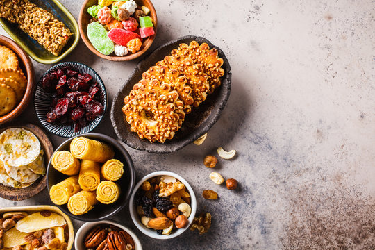 Variety of snacks and sweets on gray background. Waffles, nuts, sweets, cookies, chips and fruits, top view, flat lay.