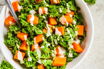 Kale and baked sweet potato salad with tahini dressing in white bowl, top view. Healthy vegan food concept.