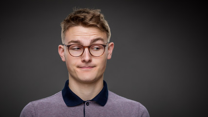 A young studious boy wearing glasses isolated on a grey background looks down at copy space