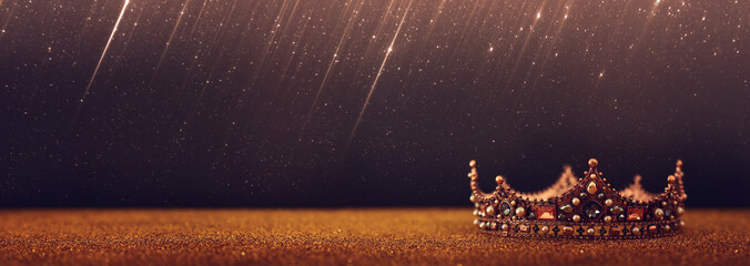 low key image of beautiful queen/king crown over gold glitter table. vintage filtered. fantasy medieval period