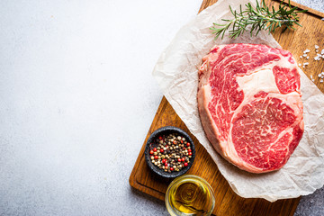 Raw fresh meat Ribeye Steak and seasonings on light background, top view with copy space