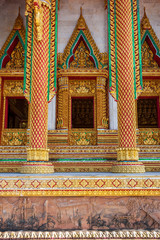 Chic gilded columns and windows of a Buddhist temple with beautiful ornaments. Sacred plots are molded from clay below. Vertical orientation.