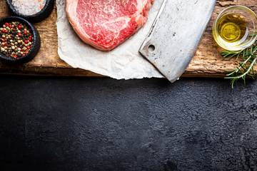 Raw fresh meat Ribeye Steak and seasonings on dark background, top view with copy space