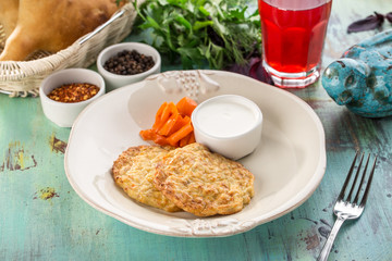 homemade cod fritters with sour cream sauce and carrot and glass of red drink on blue wooden table