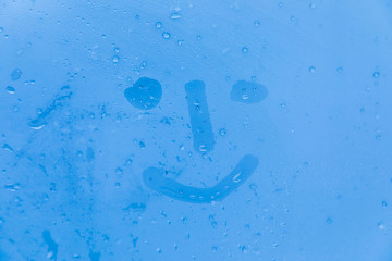 The picture or figure of the smiling face on the blue evening or morning window glass with drops 